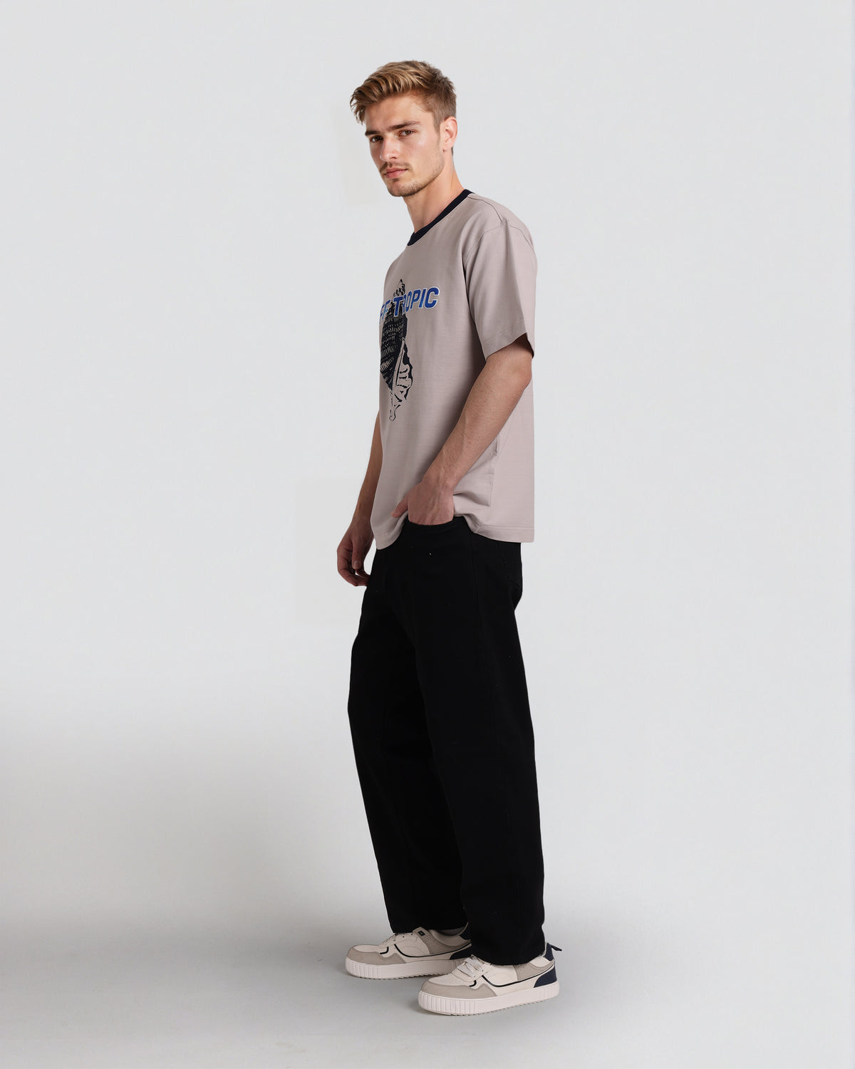 Man wearing a beige t-shirt with a graphic design and black pants on a white background