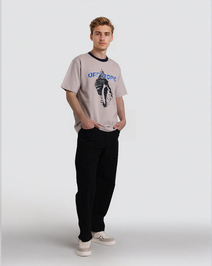 Person wearing a beige t-shirt with graphic design and text, black pants, and white sneakers on a white background